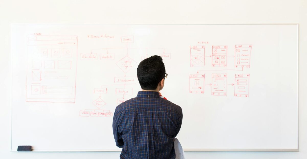 Man standing at a whiteboard planning UX design concepts in a modern office setting