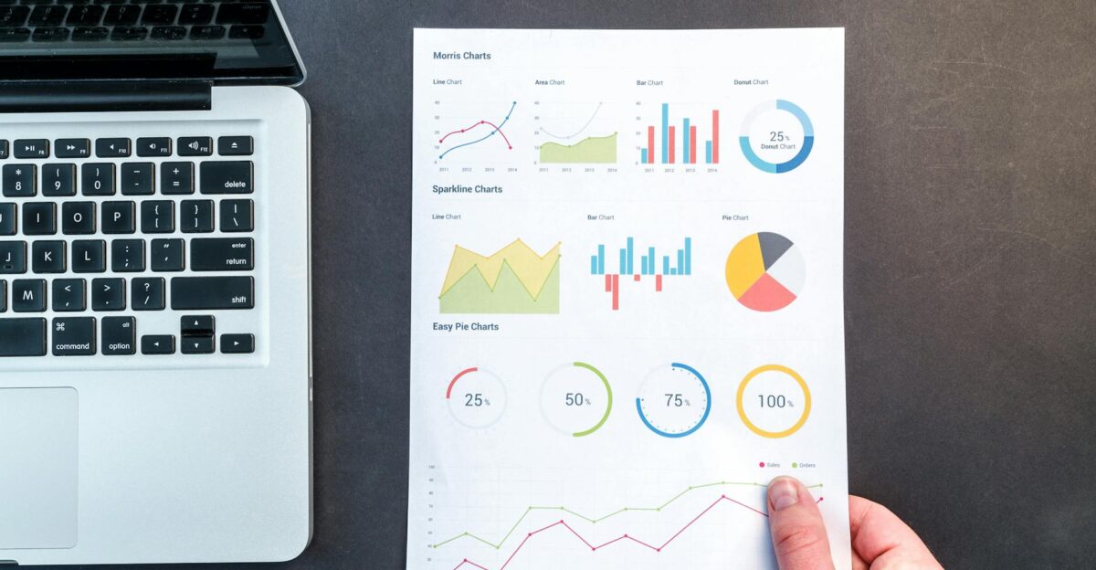 Detailed charts and graphs on a document next to a laptop representing data analysis